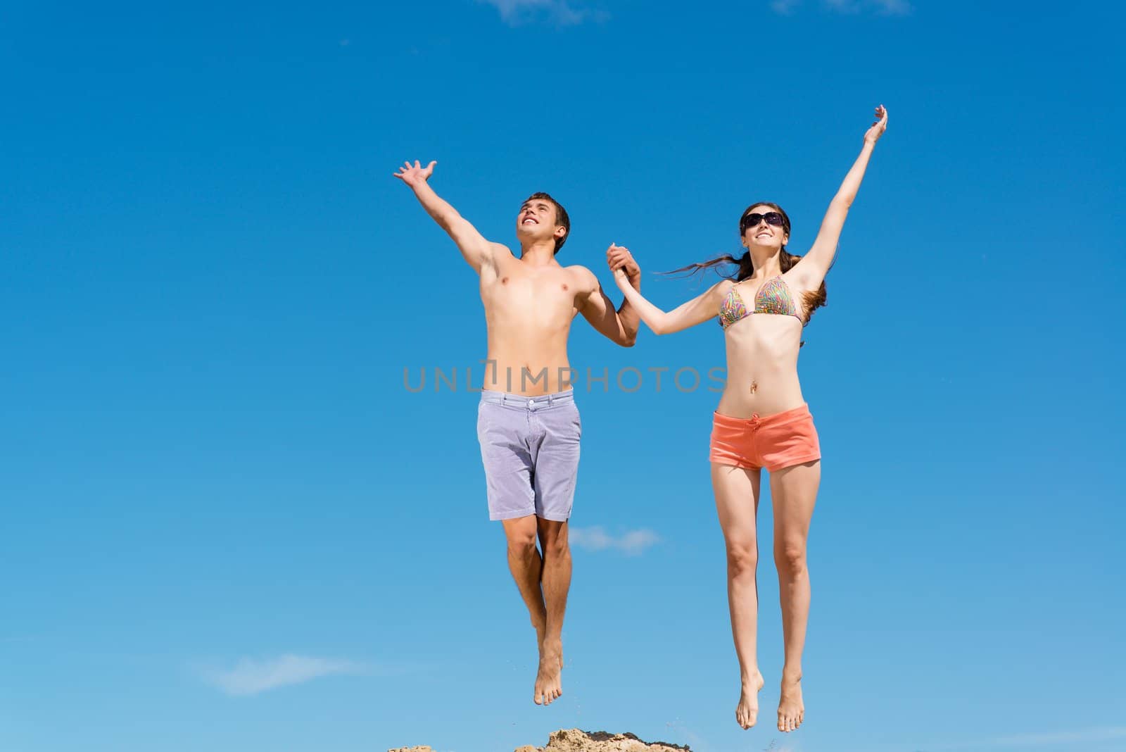 couple jumping together holding hands on a background of blue sky
