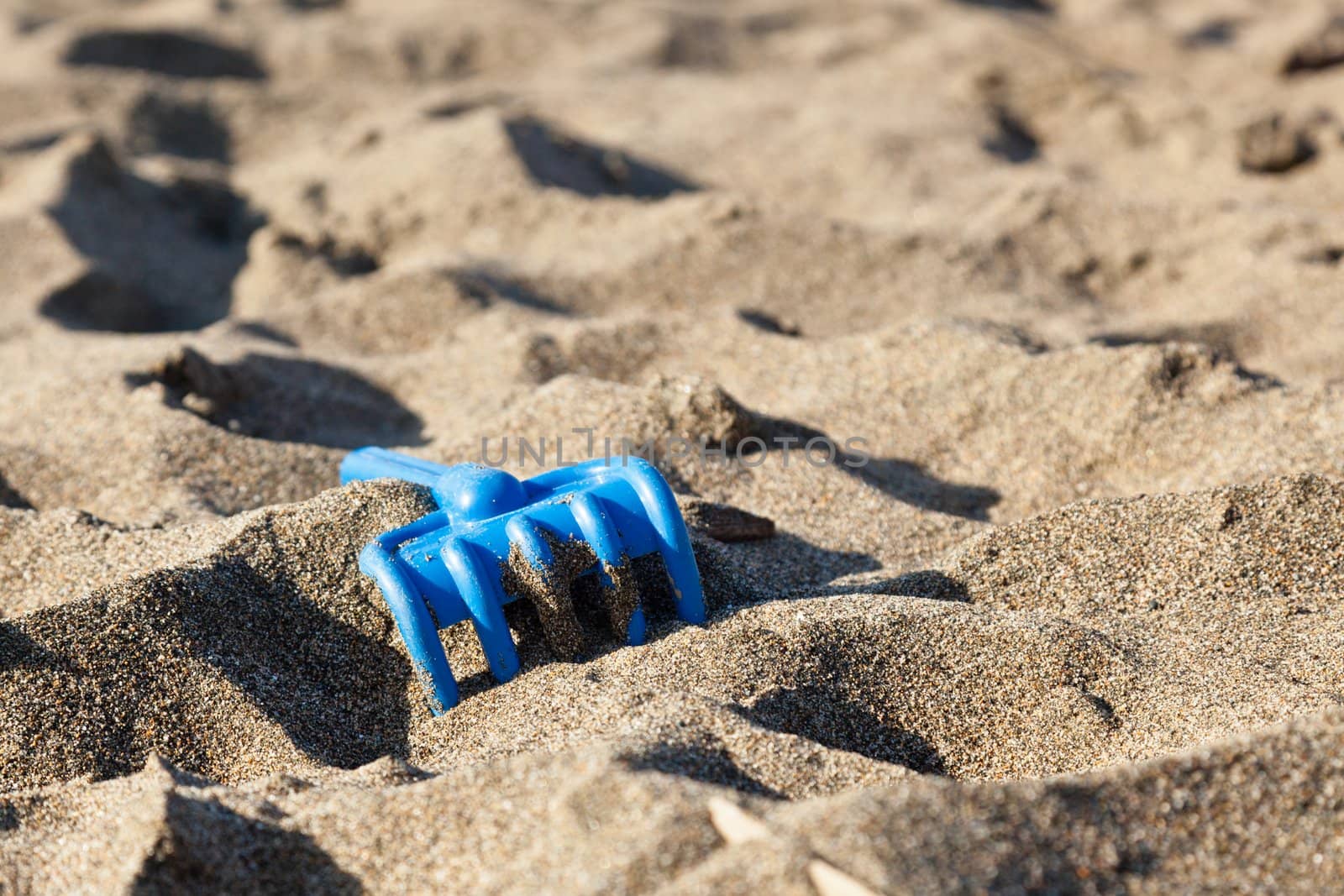 Plastic blue beach toy rake on the dark sand.
