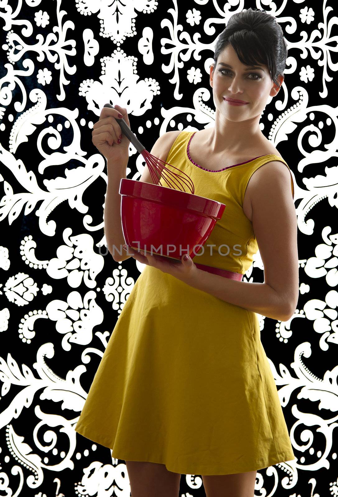 young woman in front of a black and white textured background with 60's inspired style, holding a red whisk in a red bowl