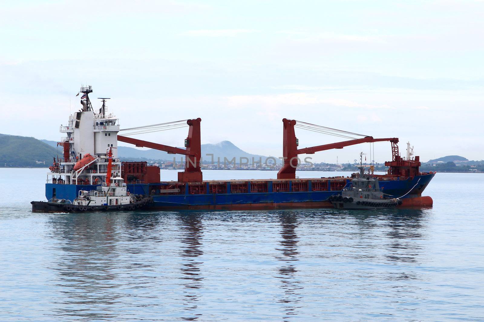 Tugboat assisting bulk cargo ship to harbor quayside by rufous