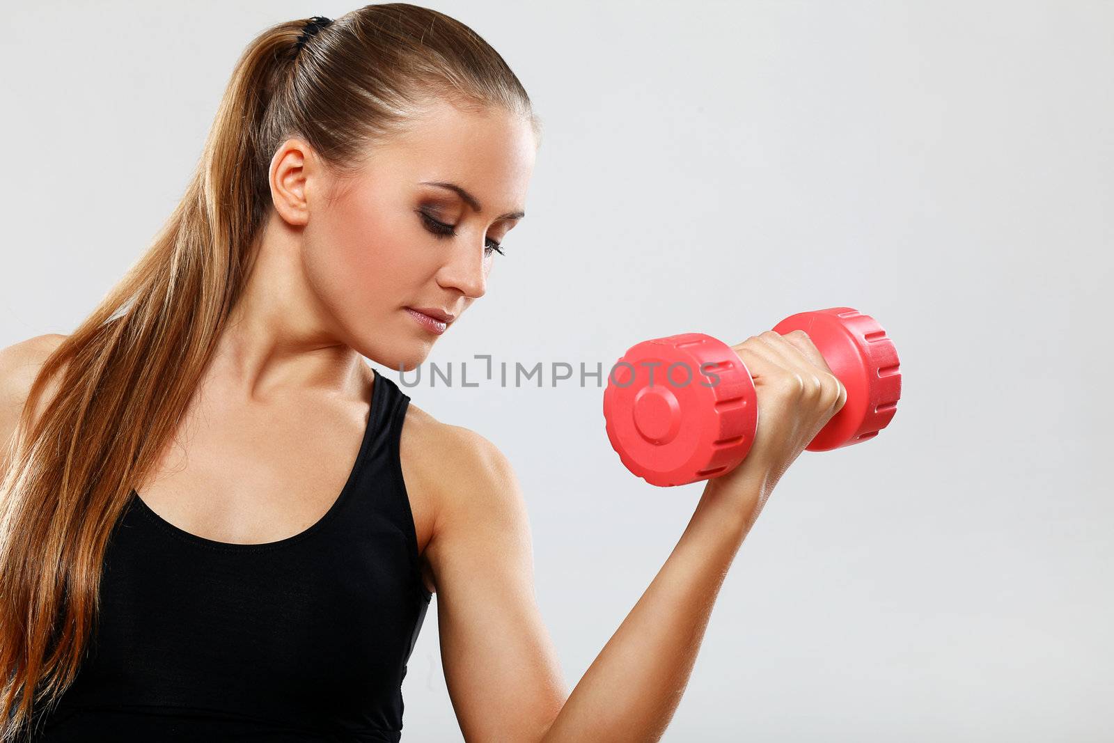 Beautiful brunette working out with dumbbells over gray background