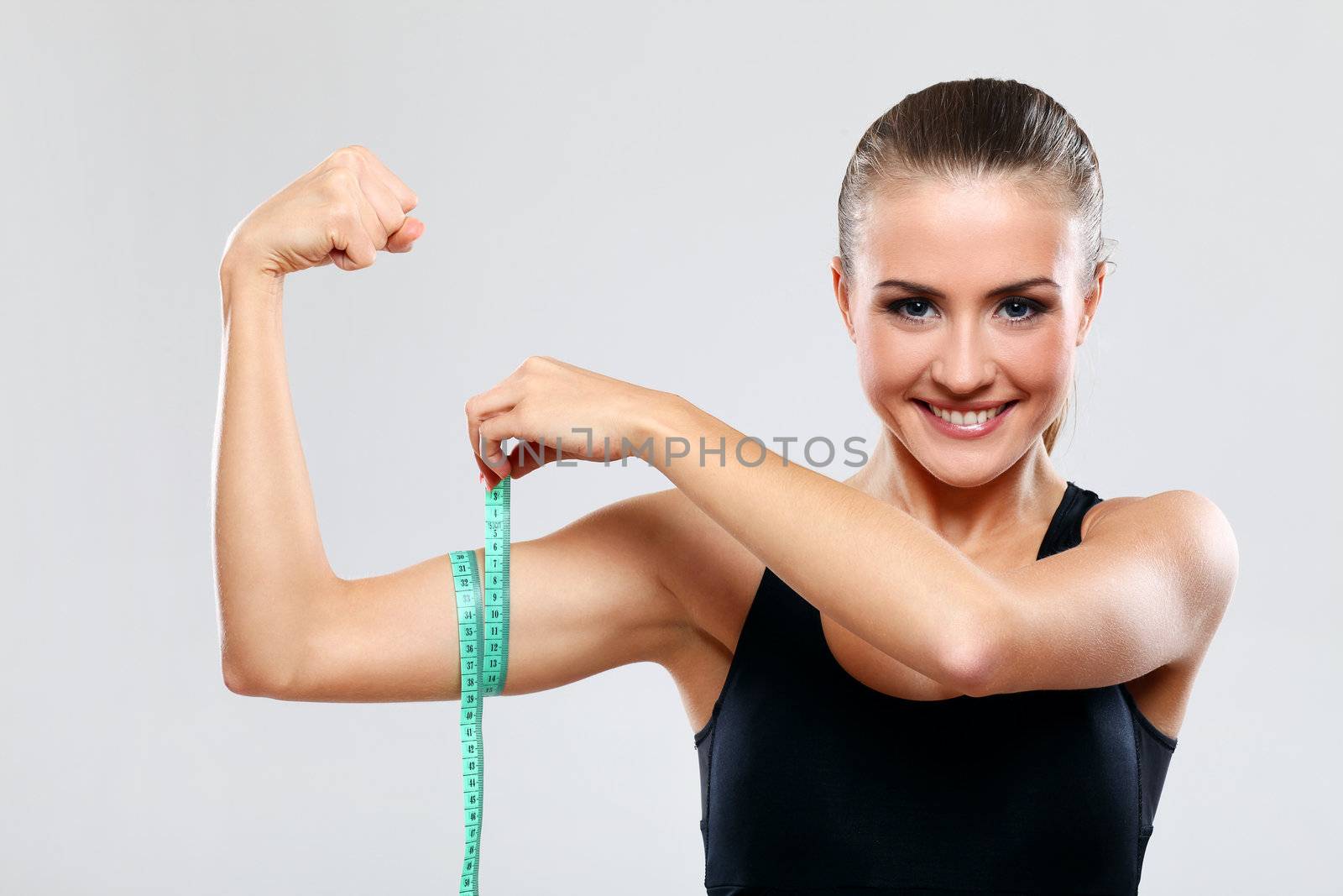 Beautiful fitness girl measure her biceps with a ruler over grey background