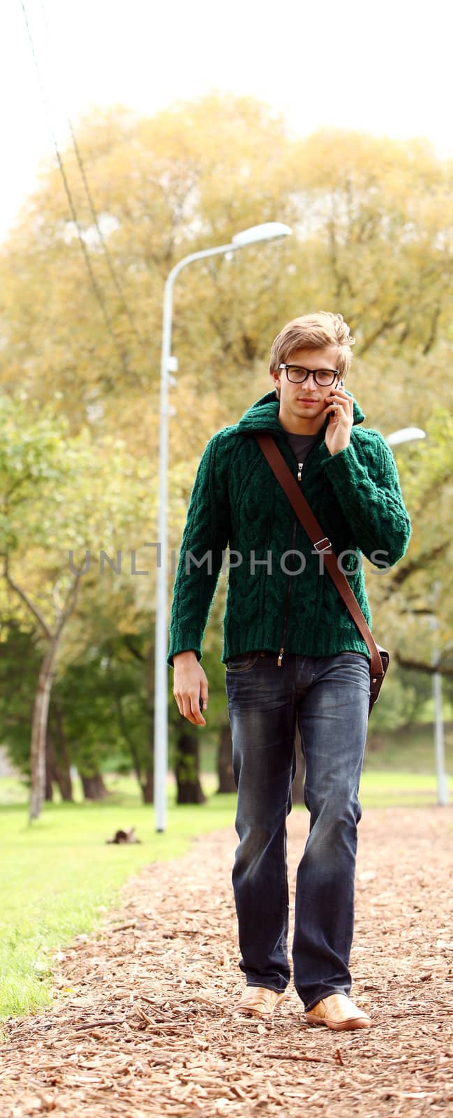 Young and handsome guy in glasses walking with cellphone in the autumn park