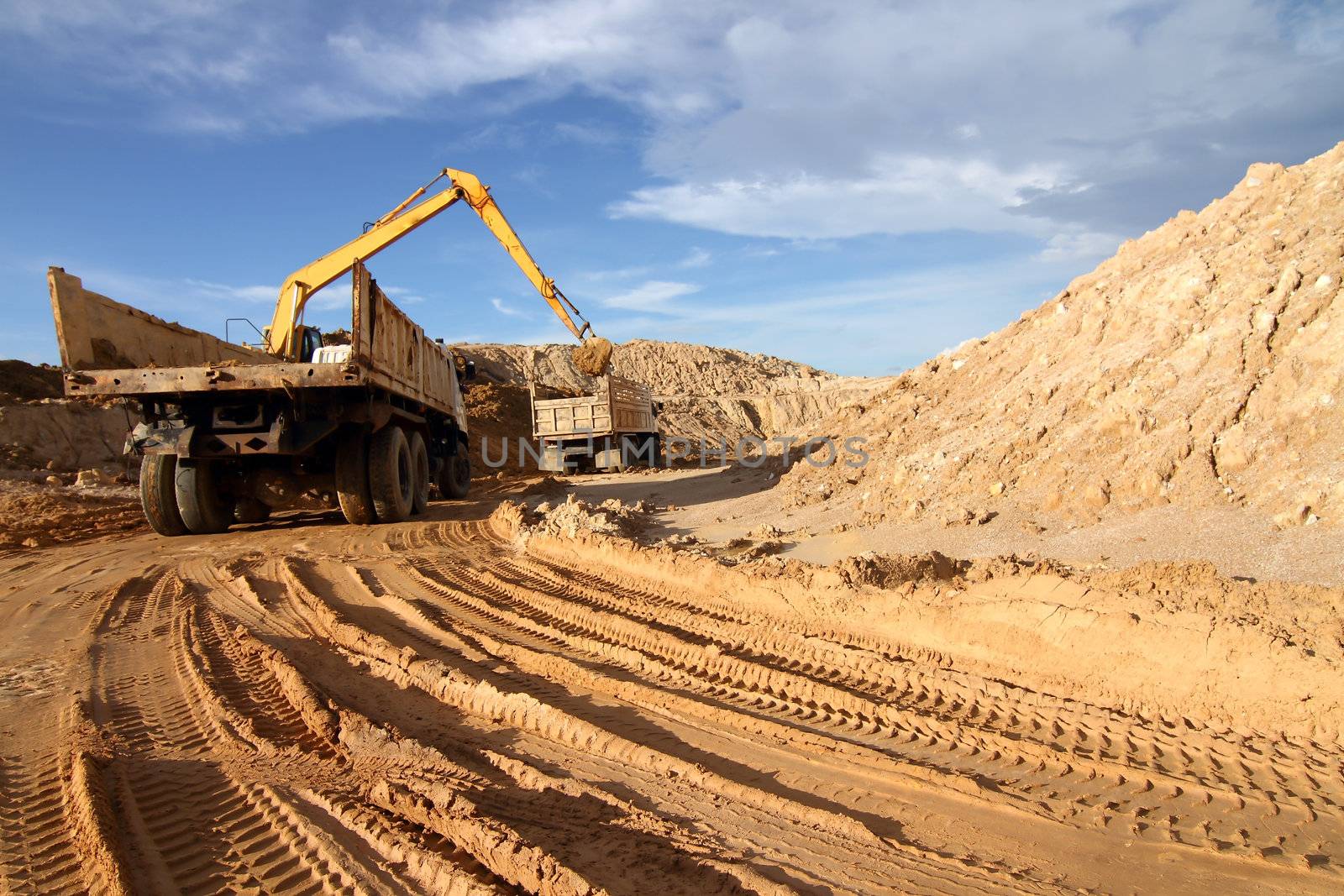 Heavy excavator loading dumper truck with sand in quarry over blue sky