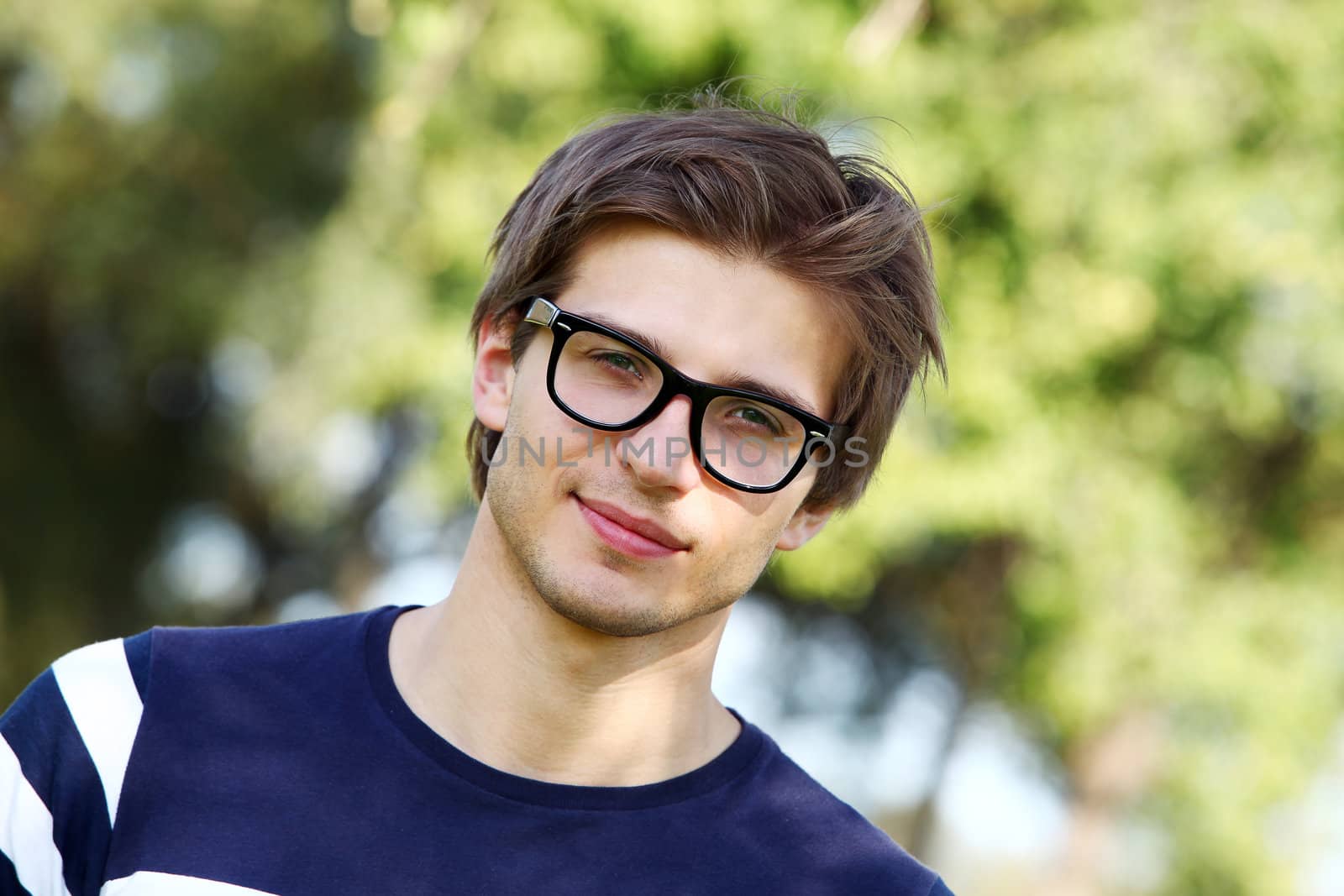 Portrait of young and smiling cute man with glasses in park