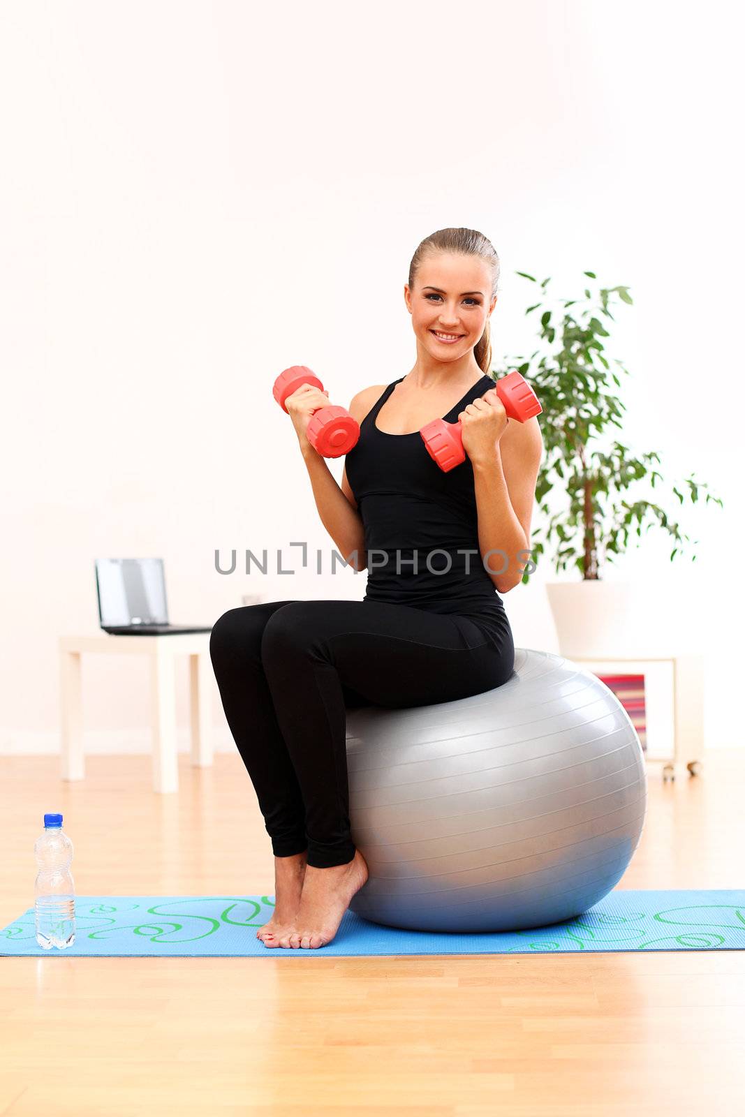 Happy and young woman working out with dumbbells on fitness ball at home