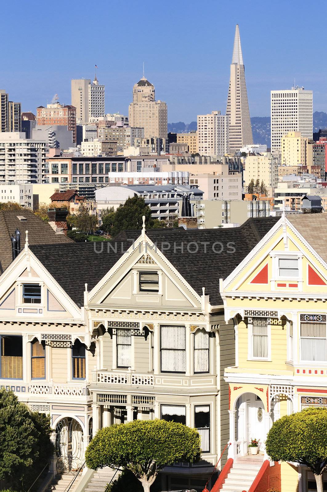 The Painted Ladies of San Francisco, California sit glowing amid the backdrop of a sunset and skyscrapers. 