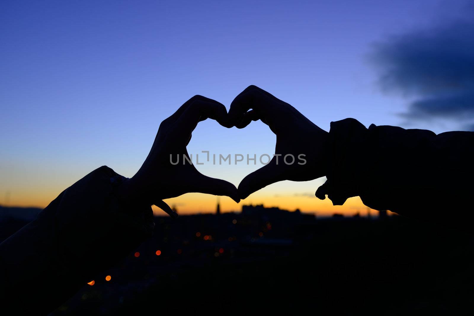 Silhouette of hands in form of heart when sweethearts have touched in autumn with sunset at city background