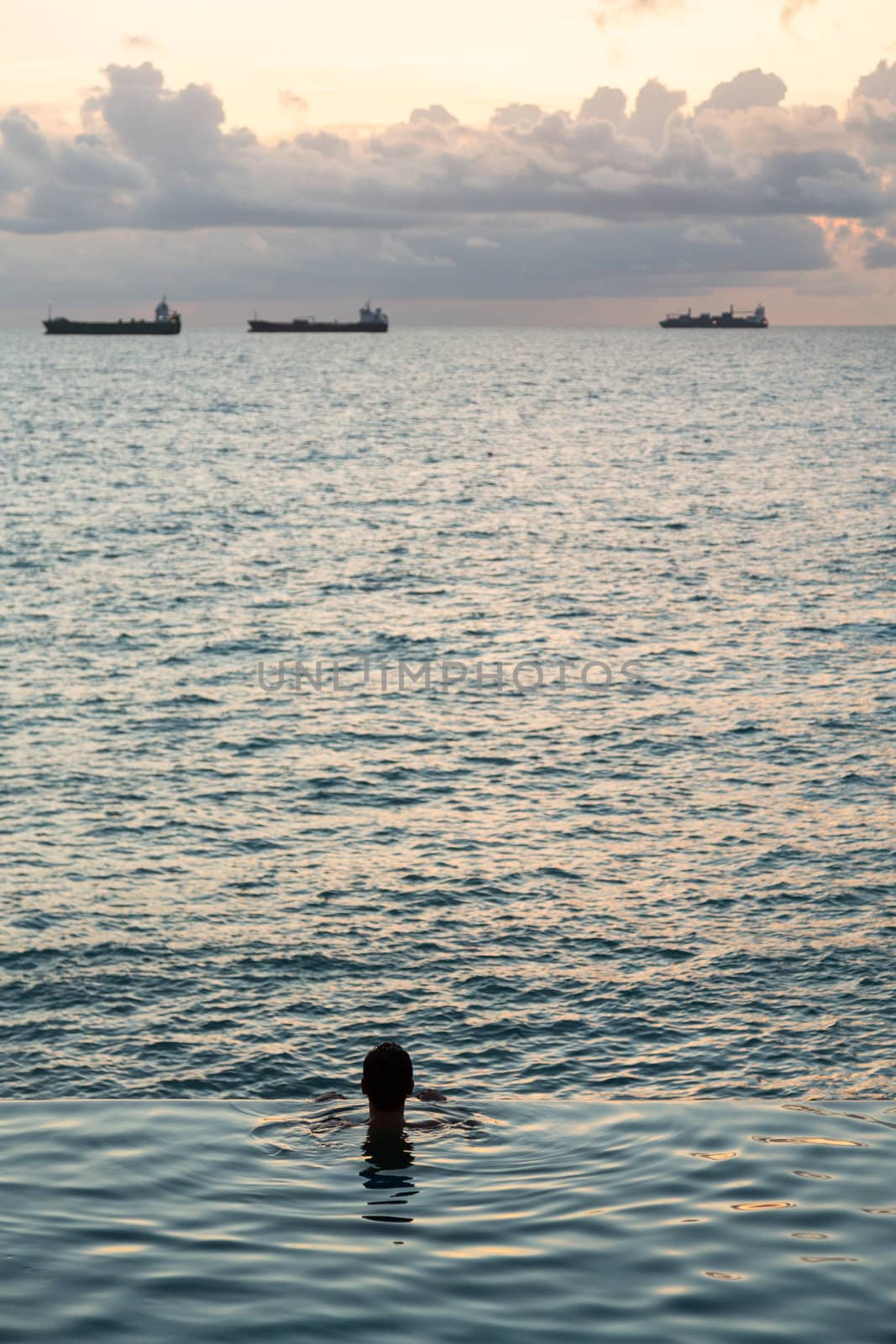 Silhouette of person head at the edge of infinity swimming pool overlooking ocean at sunset