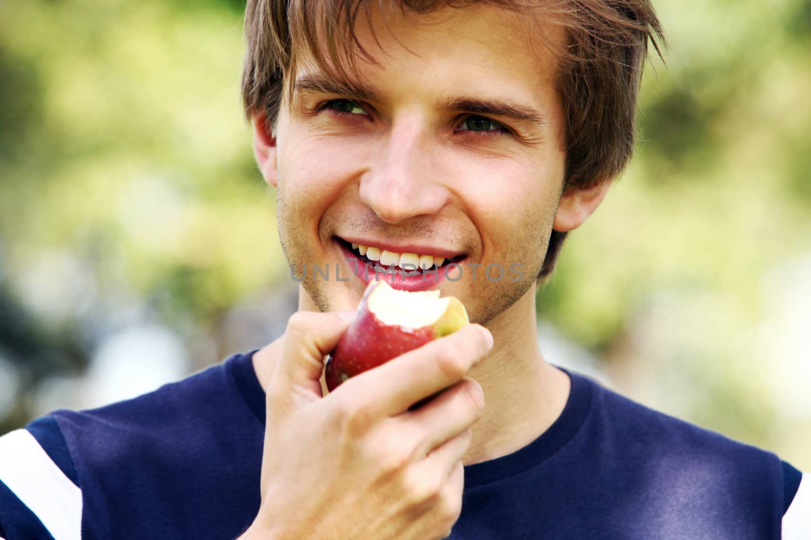 Portrait of young and smiling cute man with apple in park