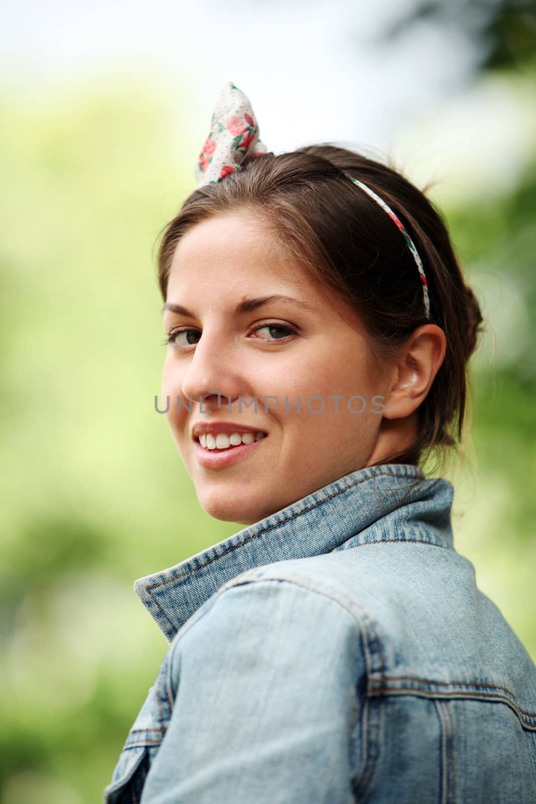 Portrait of young smiling woman in jeans jacket standing in park