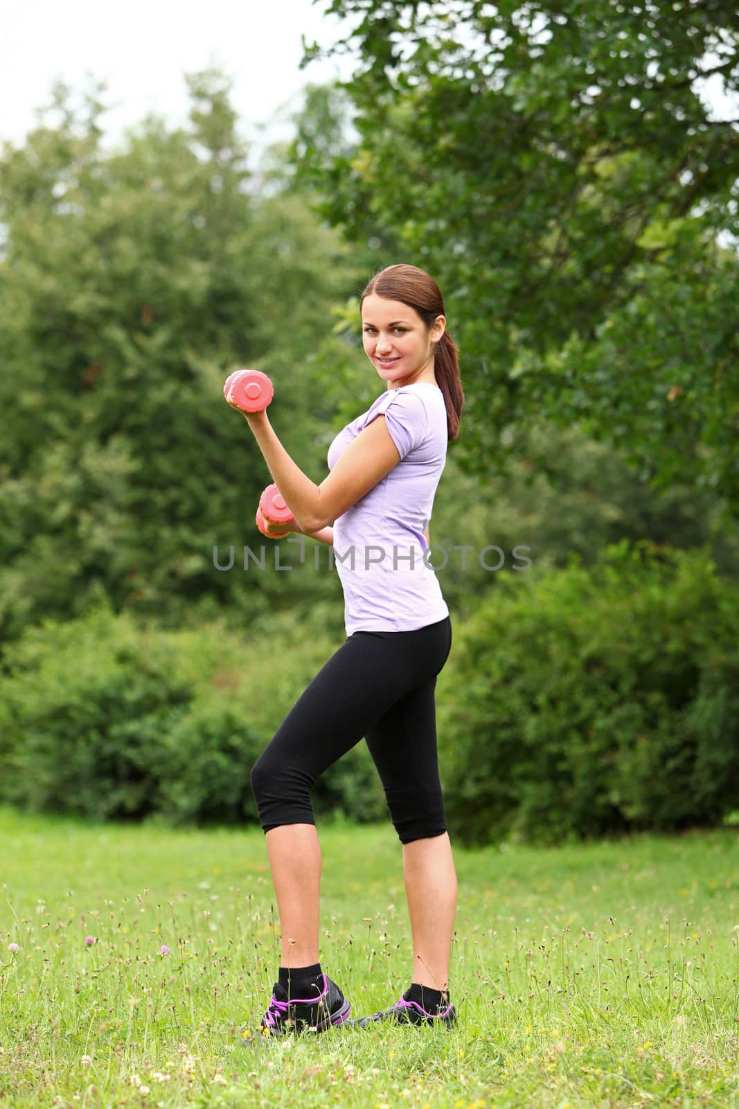 Young woman doing her fitness exercises with red dumbbells in the park