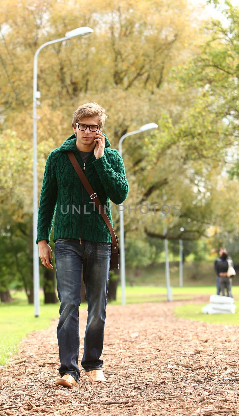 Young and handsome guy in glasses walking with cellphone in the autumn park
