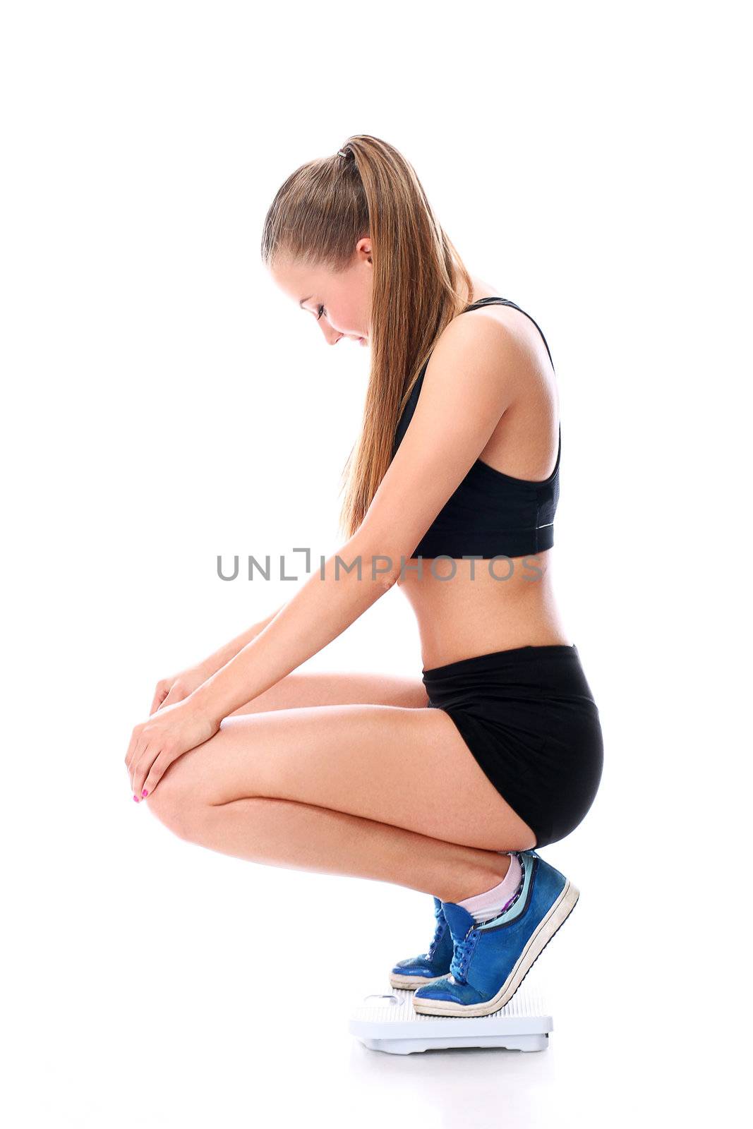 Young and beautiful fitness girl on the scales over white background