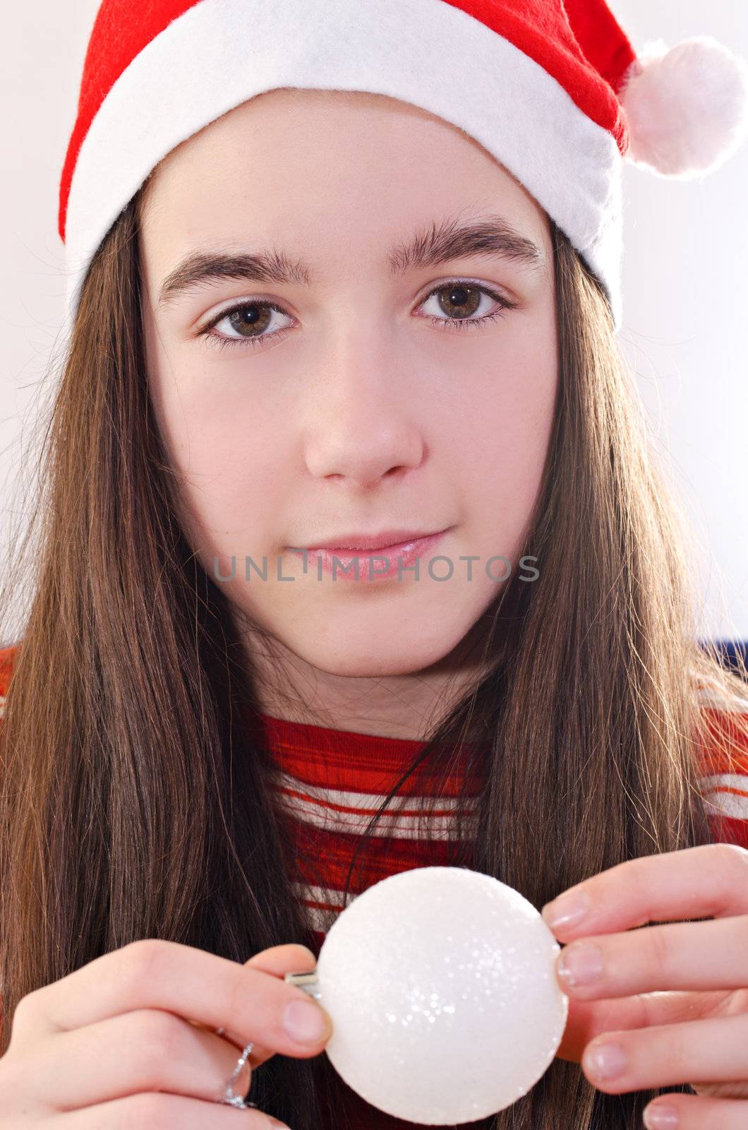 Christmas portrait of young girl holding bauble and wearing red cap, eye contact, vertical shot