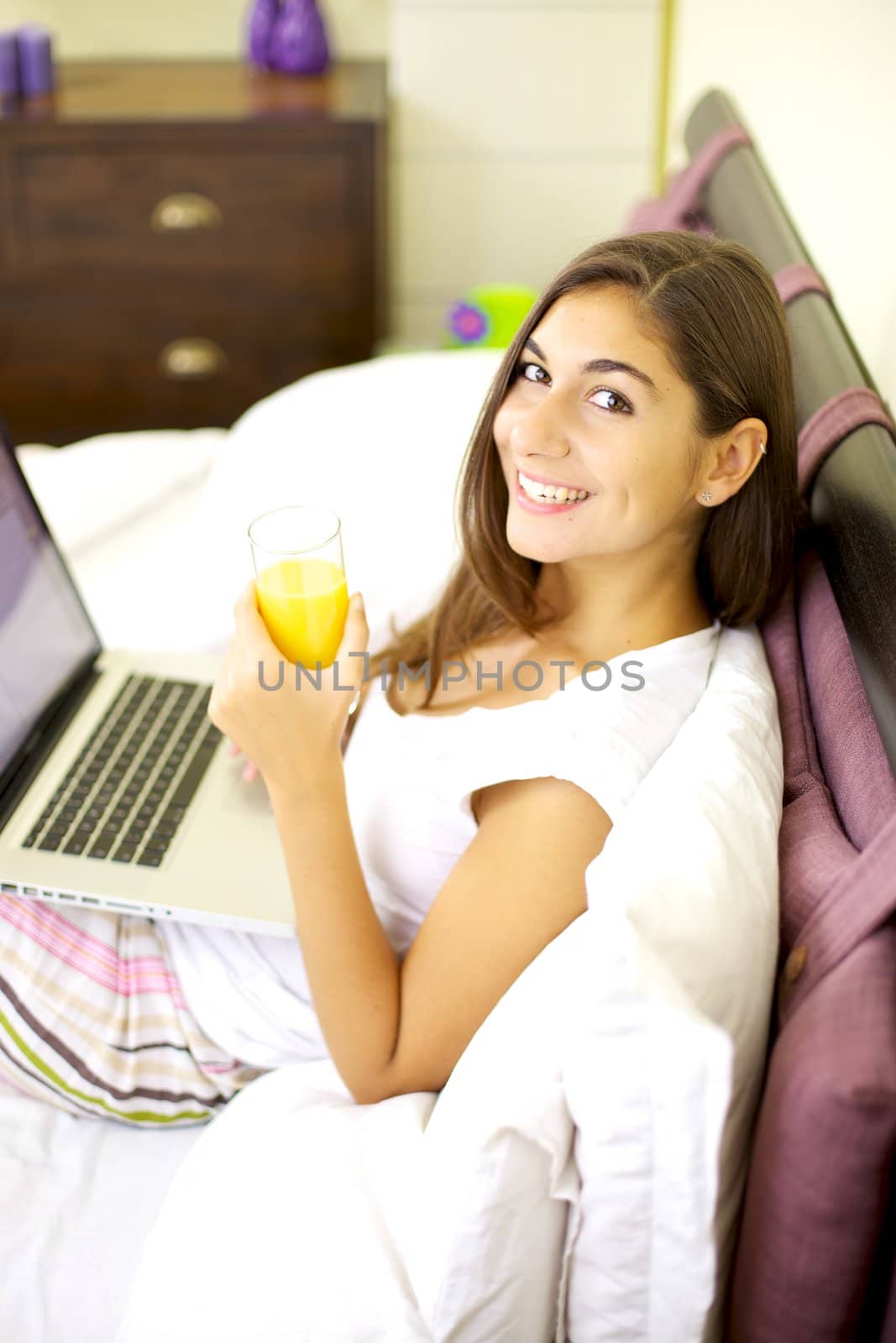 Beautiful smiling girl with computer and orange juice in bed