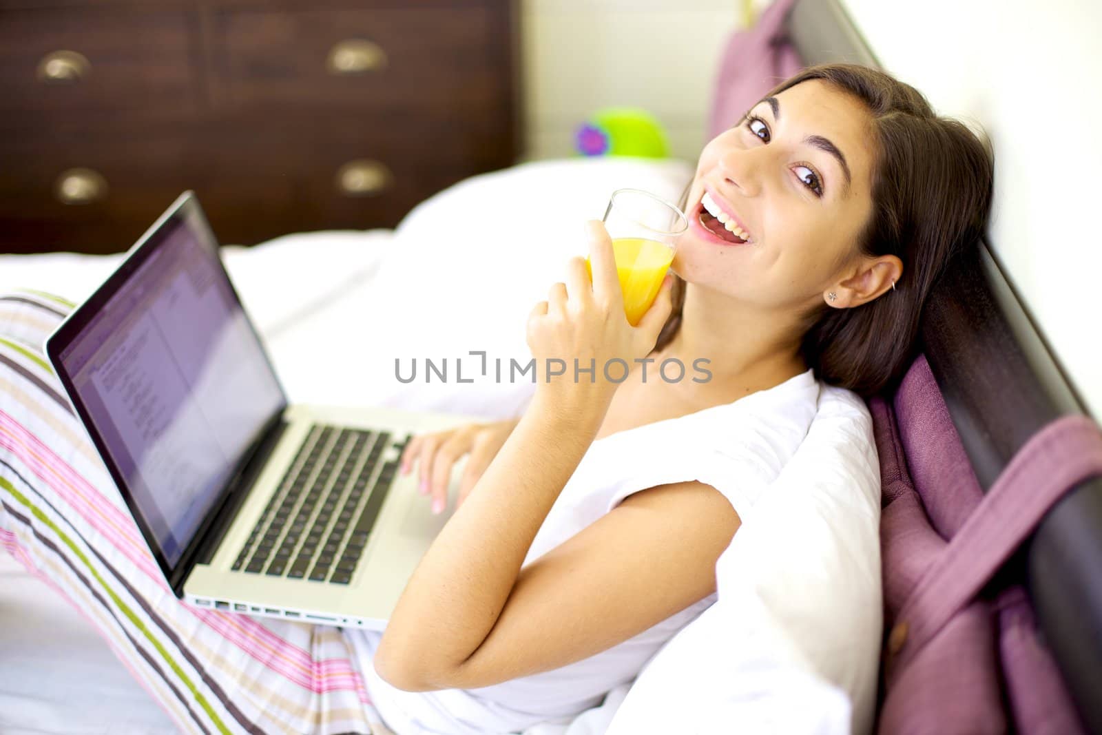 Smiling happy woman working in bed drinking juice by fmarsicano