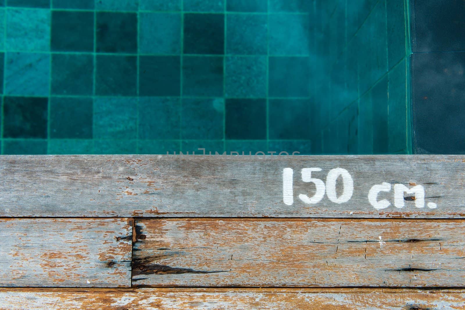 Swimming pool water depth sign on wooden platform, taken on a vertical angle.