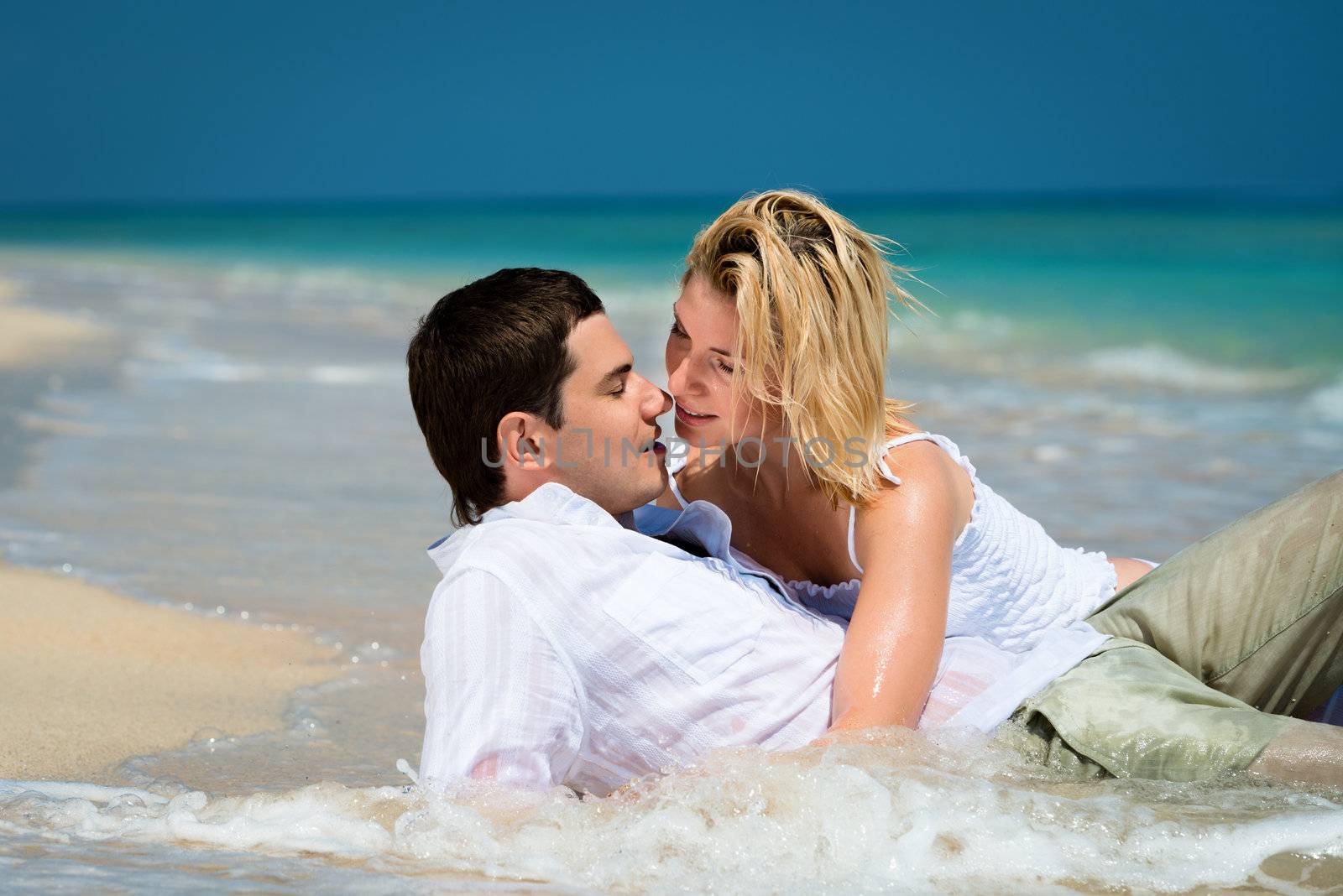 Kissing young couple lie on sand of a tropical beach with blue sea on background