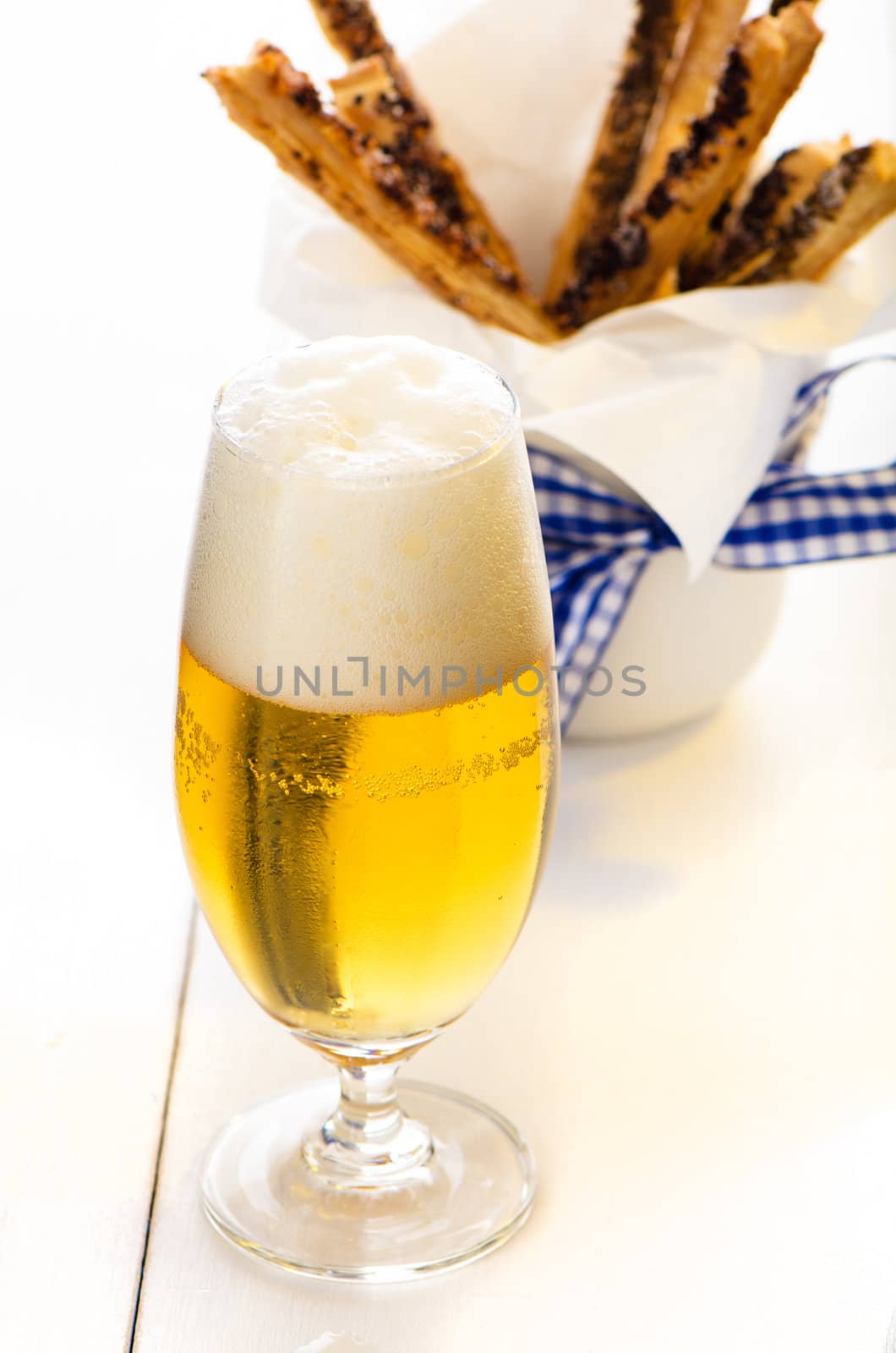 A glass of beer and spicy puff pretzel sticks in background on white wooden table