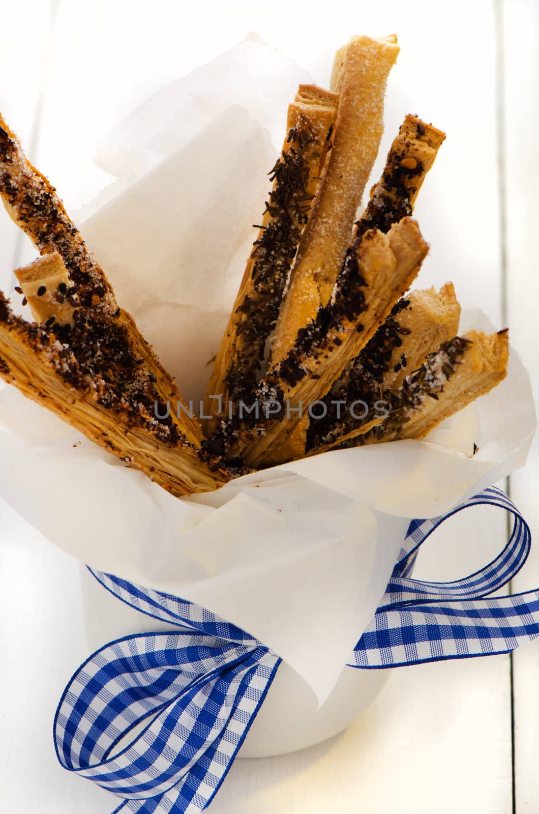 spicy puff pretzel sticks in a white cup with a blue ribbon as decoration on white wooden table