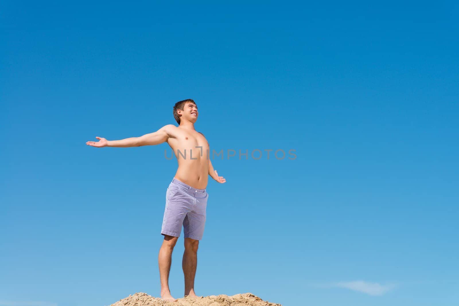 shirtless man spread his hands against the blue sky