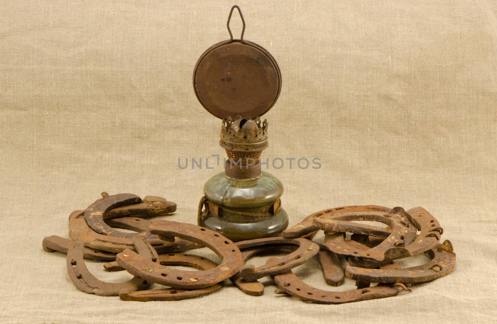 rusty retro kerosene lamp and horse shoes on linen material background