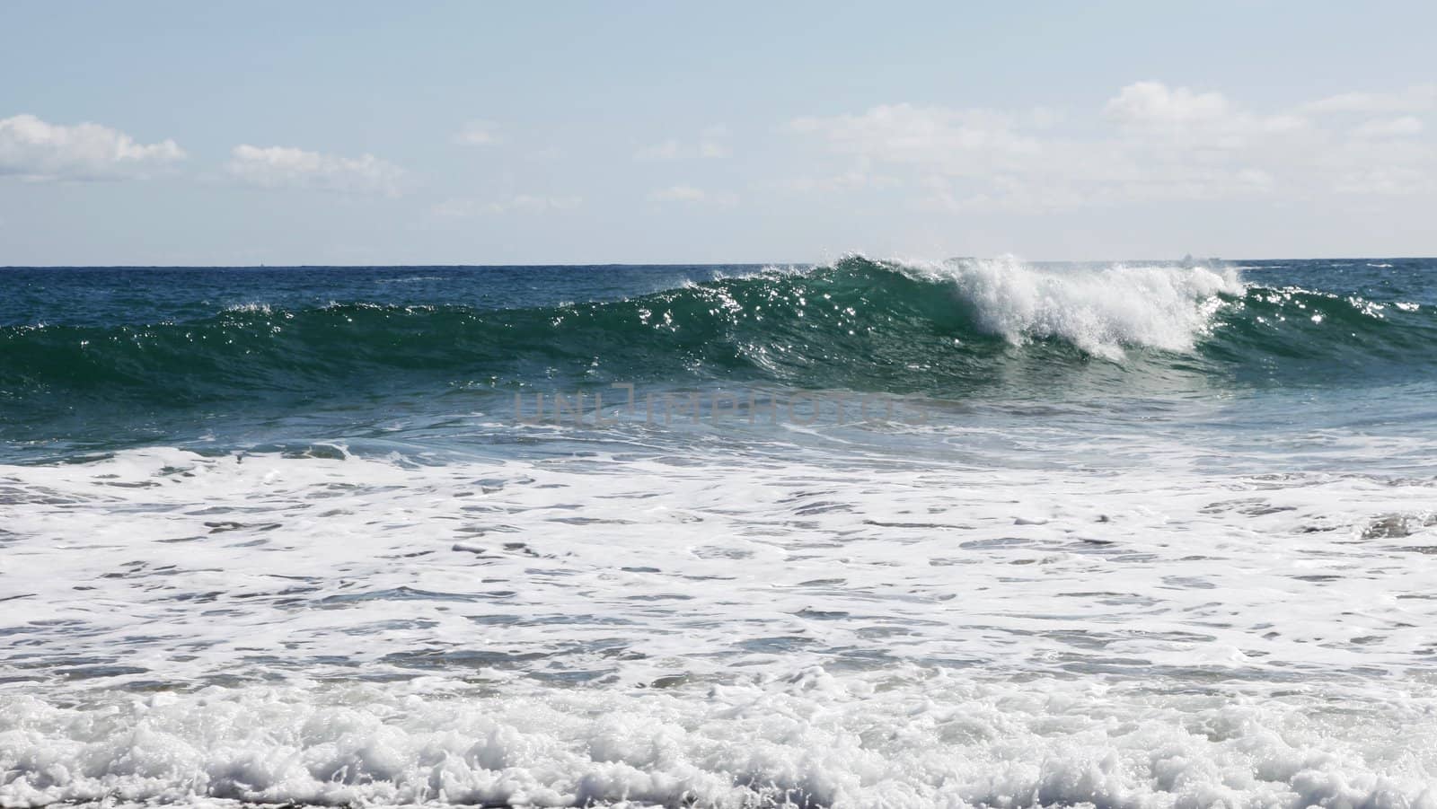 Rolling breaking blue wave with white surf