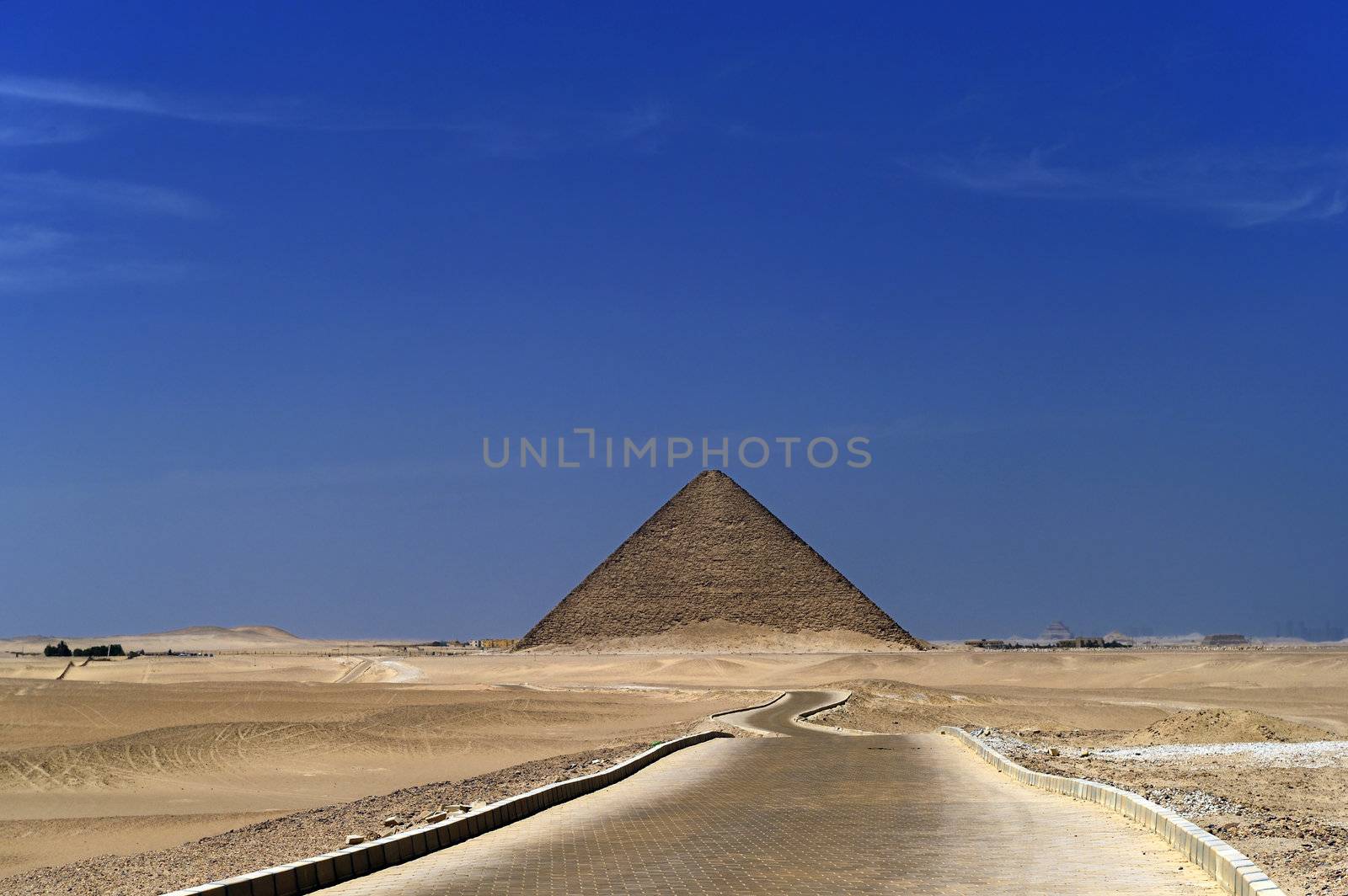 A row of camels transport tourists in front of all of the Dakshur Pyramids in Cairo, Egypt