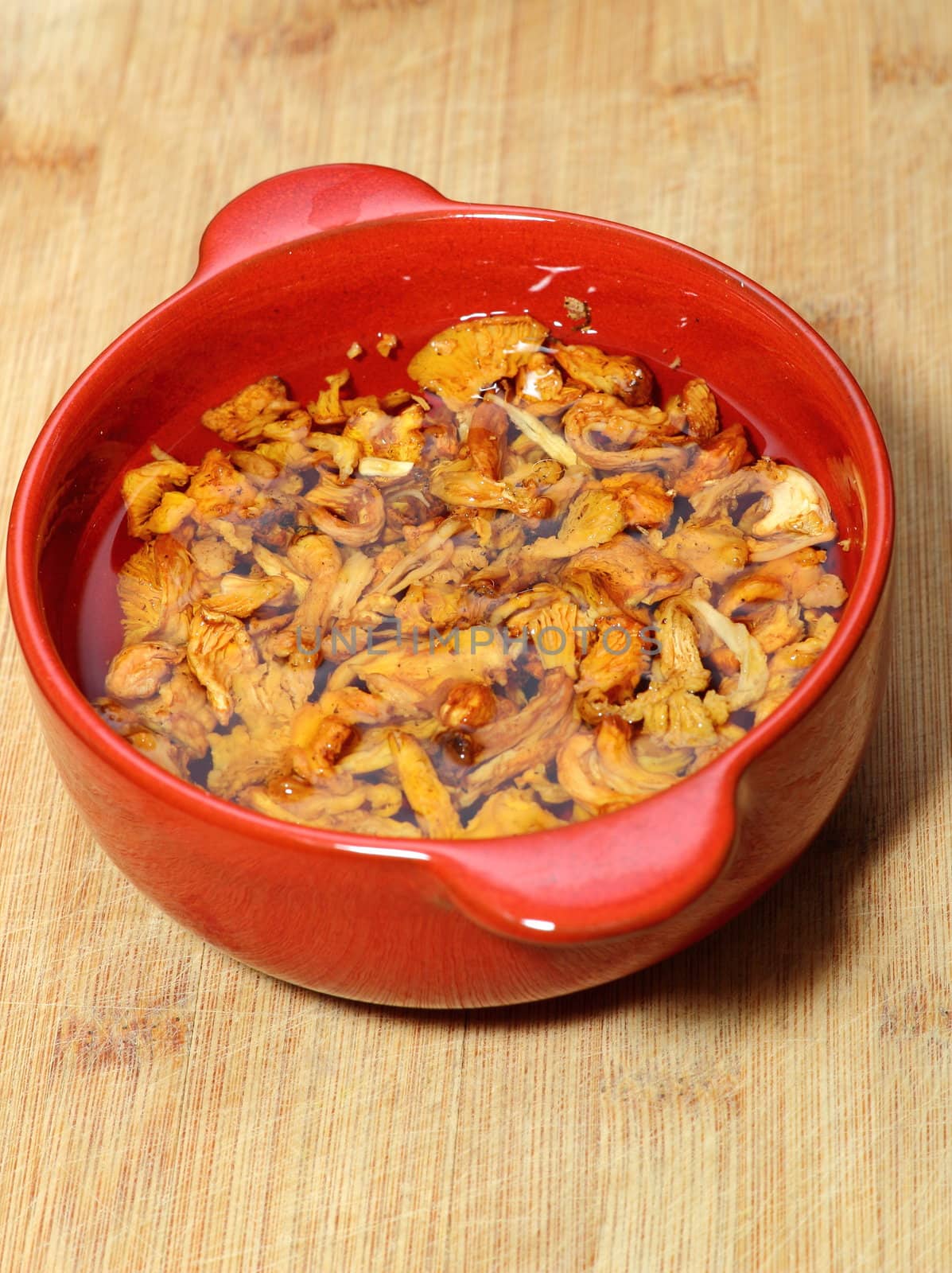 yellow mushrooms ( cantharellus cibarius ) left in water in a red bowl