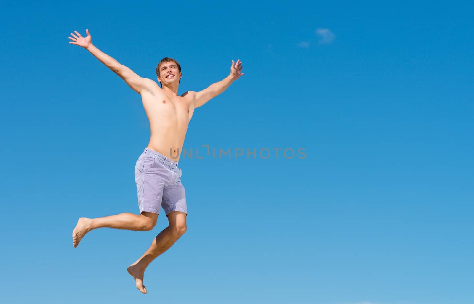 happy young man jumping on a background of blue sky, spreading his hands