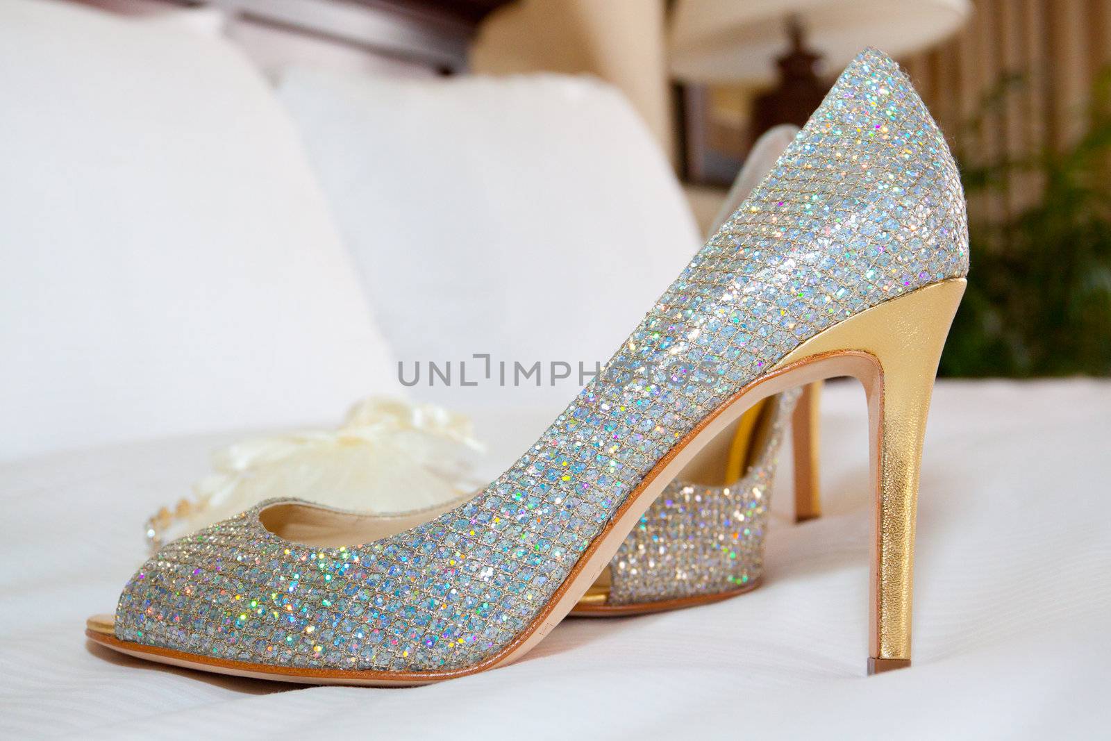 A bride's shoes sparkle while setting on the bed before a wedding ceremony.