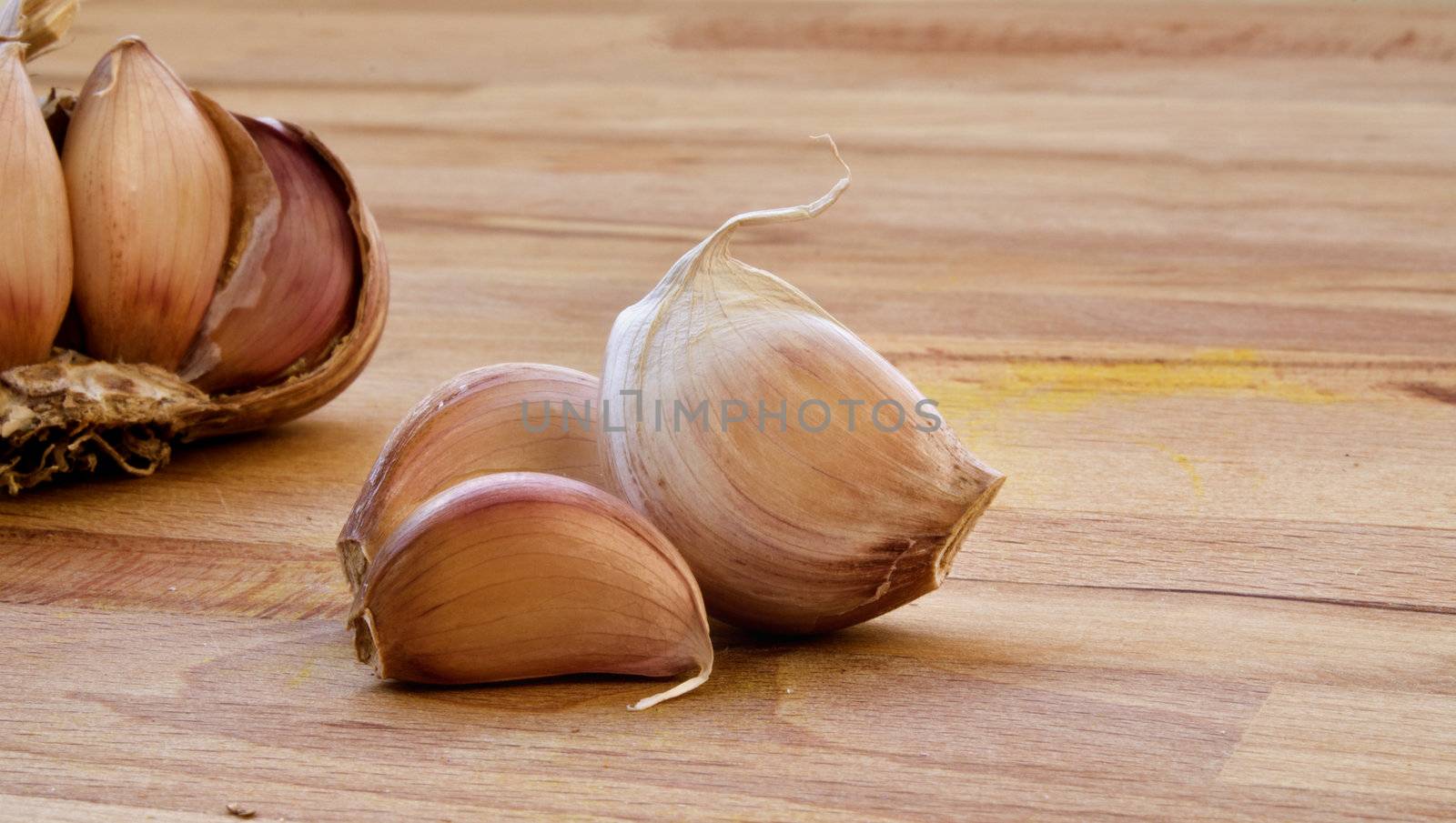 Macro of three isolated clove of garlic on a wood table with garlic behind 