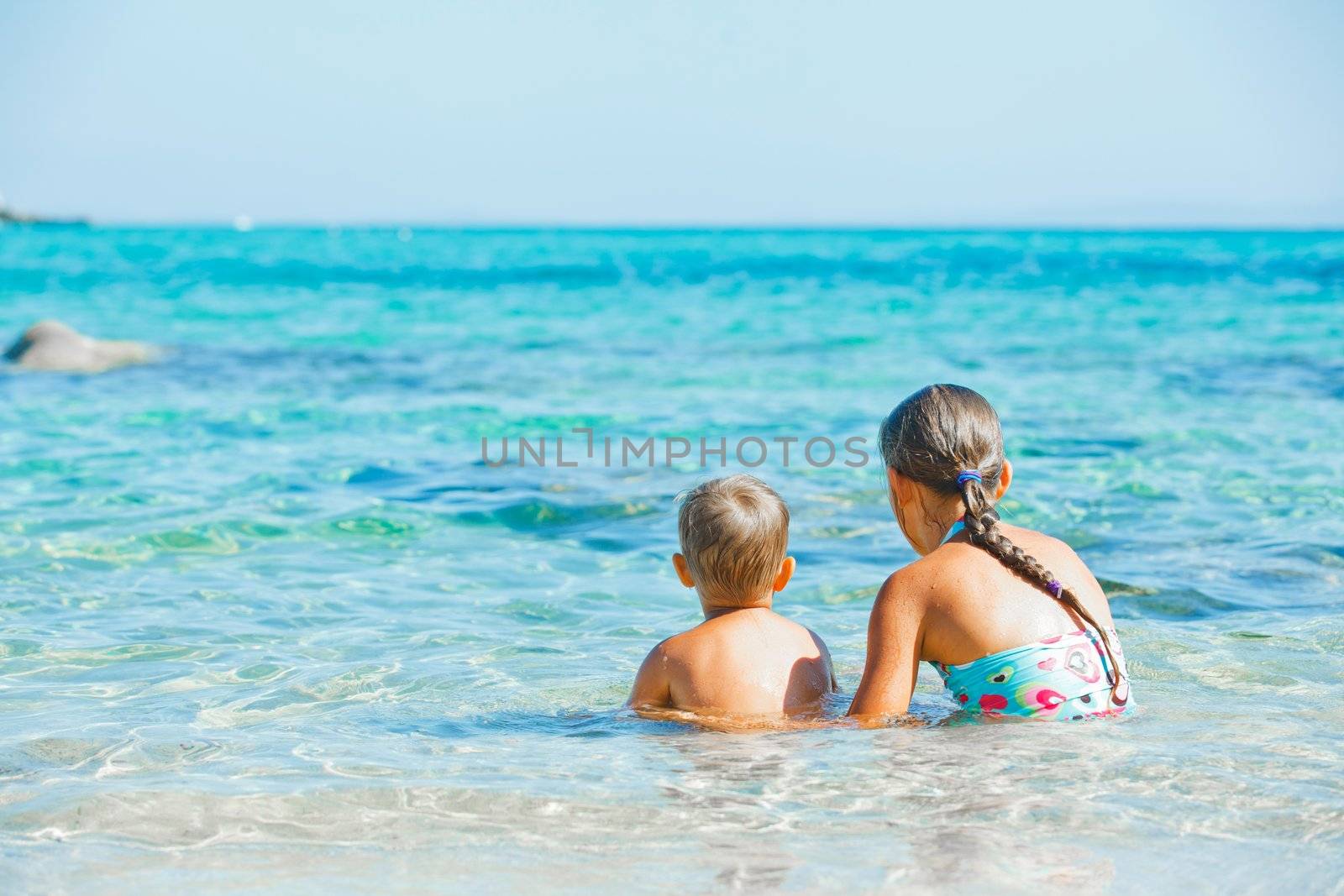 Back view of sister and brother playing and swimming in the transparent sea