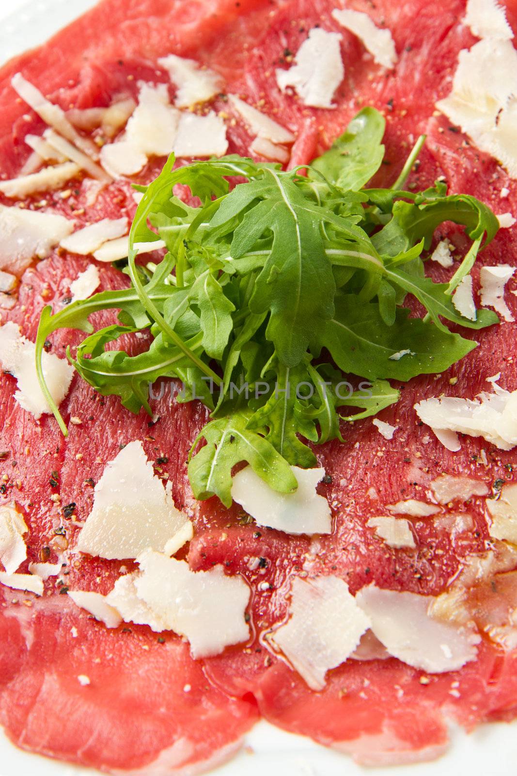 white dish with carpaccio of beef on arugula over white background