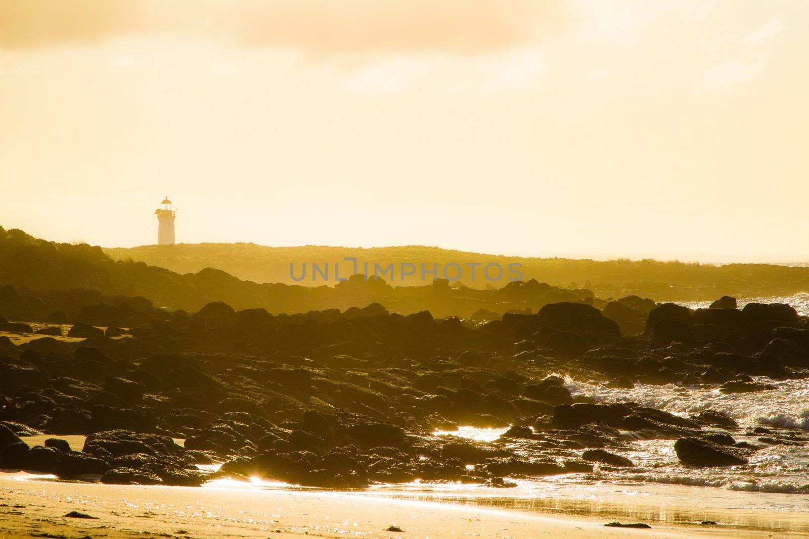 Port Fairy lighthouse beach sunrise with sea fog roll in over black volcanic rock