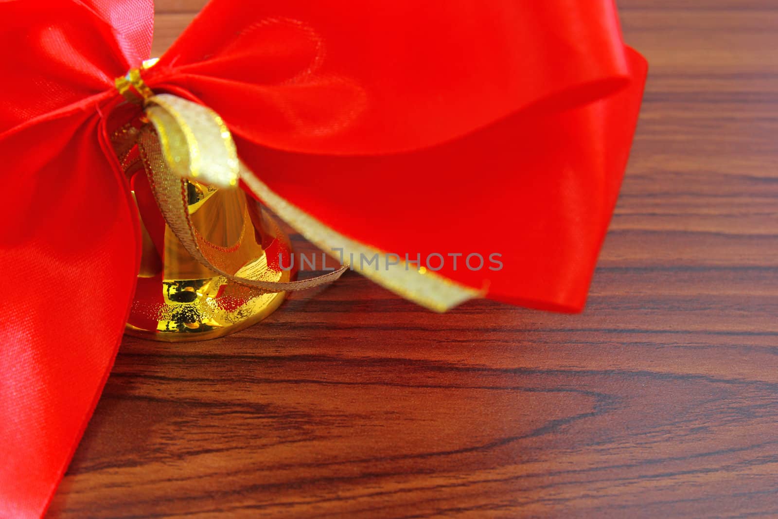 Bell with red ribbon over wooden background 