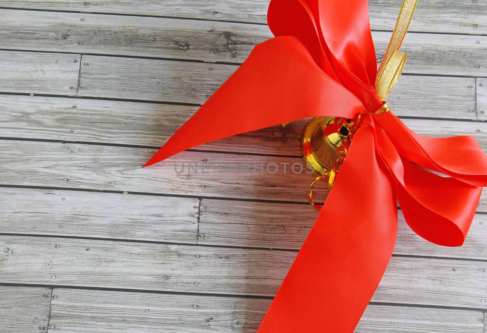 Bell with red ribbon over wooden background 