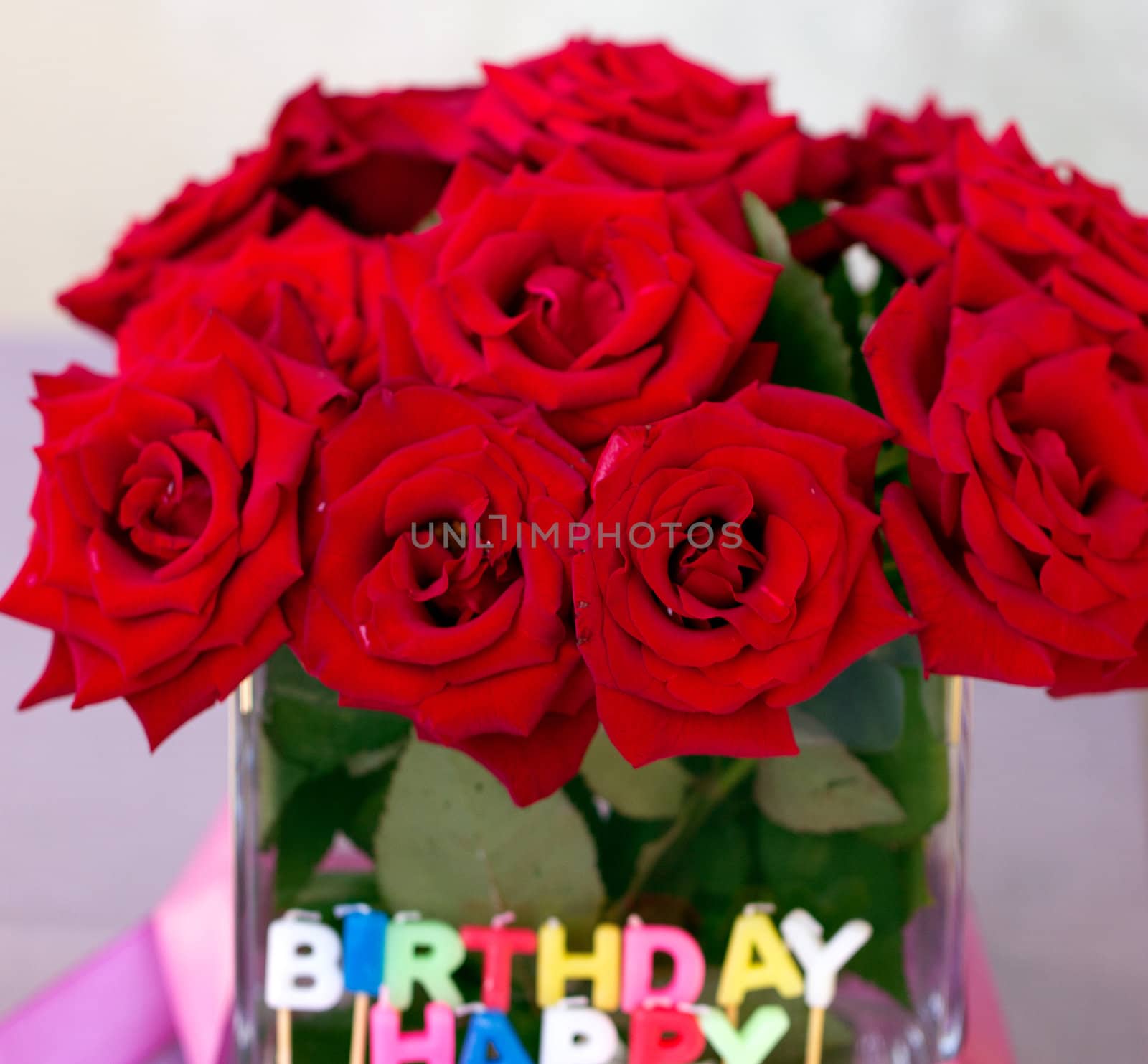 Candles of the letters "Happy birthday" in the background of a bouquet of red roses