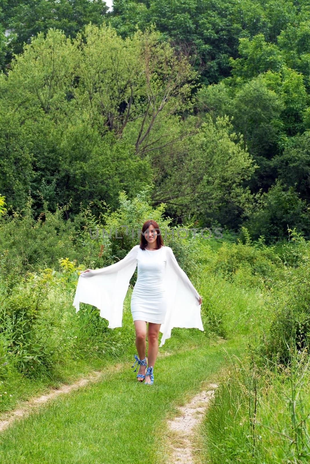 young caucasian woman in white dress walking outdoors over natural green background in nature