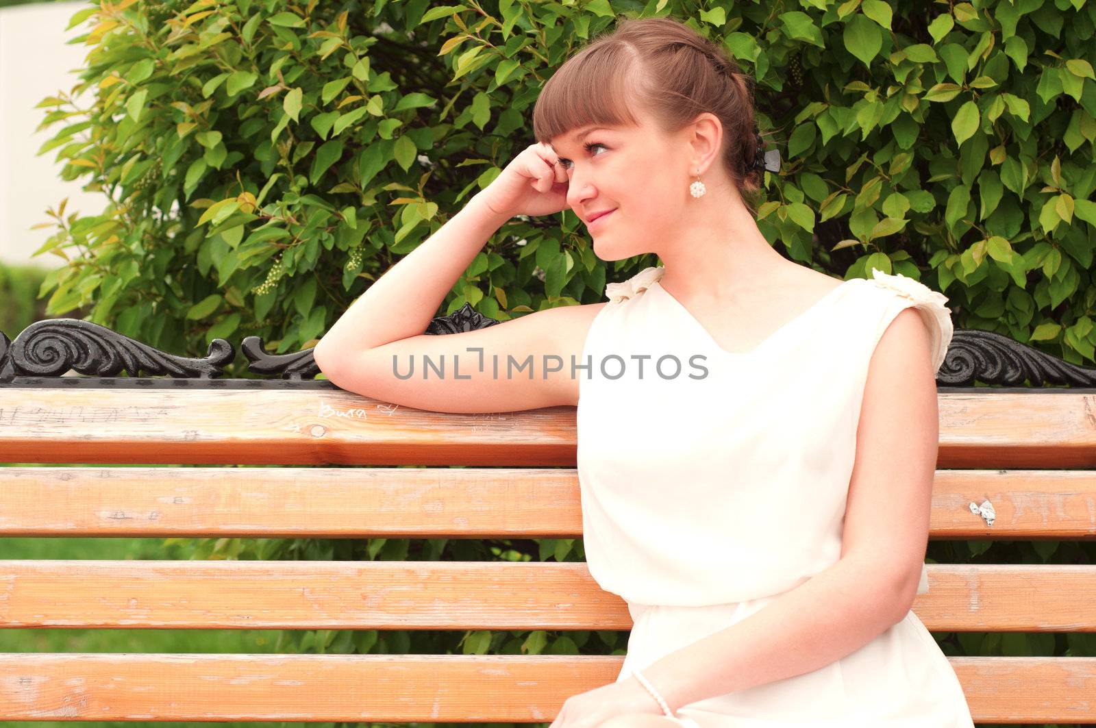 A beautiful woman is sitting on a park bench on a background of green nature
