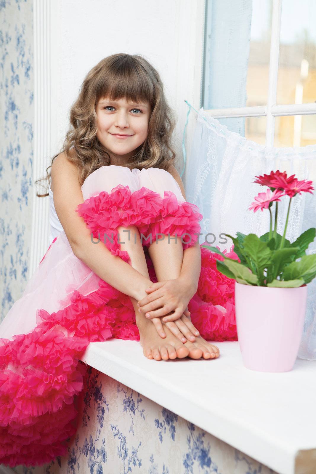 Young amazing joyful girl teenager close-up dressed luxuriant wavy skirt with frill sitting with outstretched legs on white windowsill inside room near fresh natural flower in flowerpot