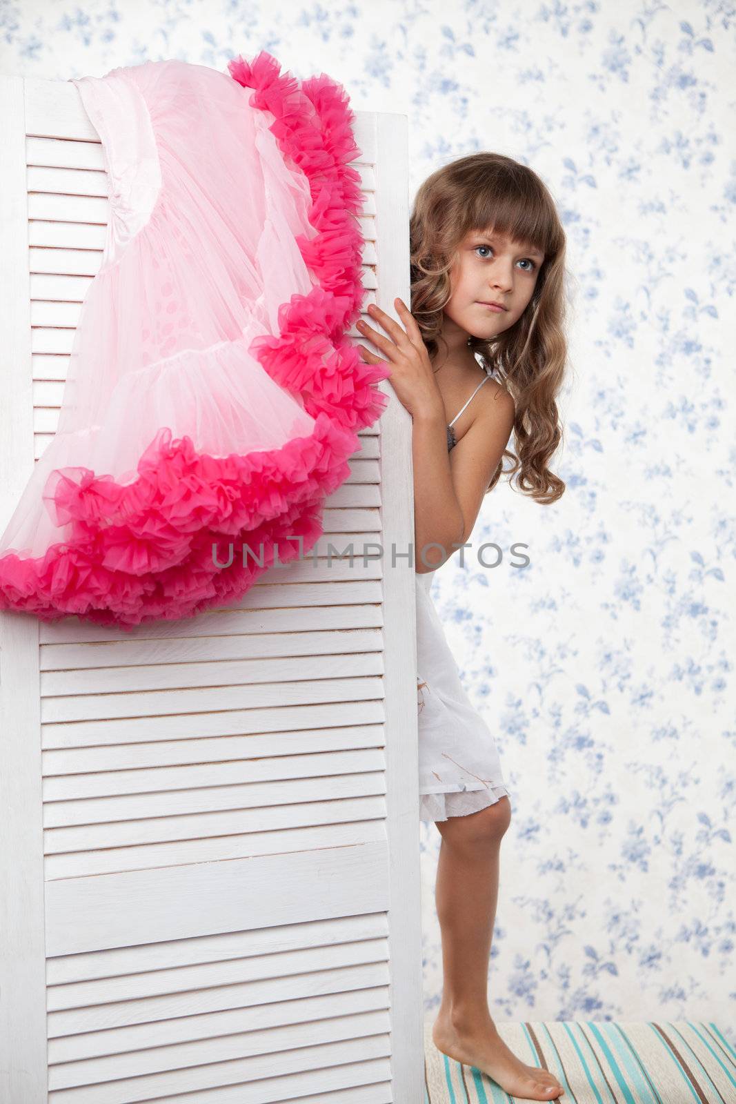 Young blond girl child with long wave hair looks out the folding screen when change of clothes