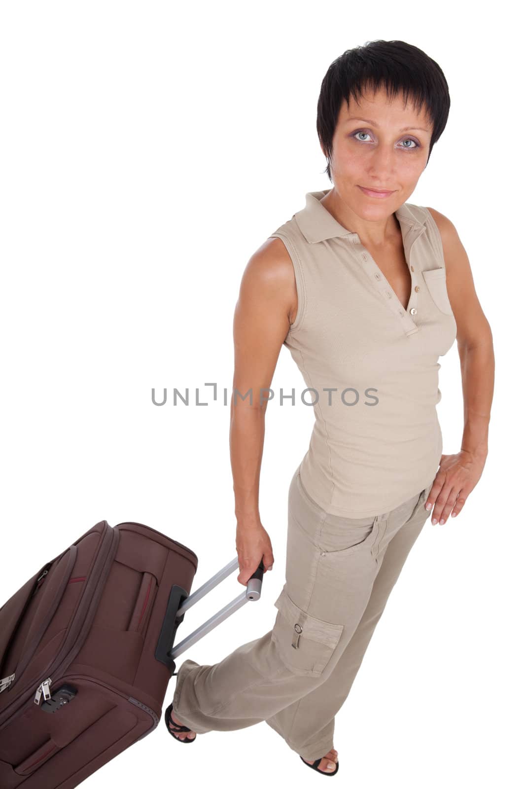 Smiling young tourist haircut woman dressed buff trouser suit stands with brown traveling suitcase isolated