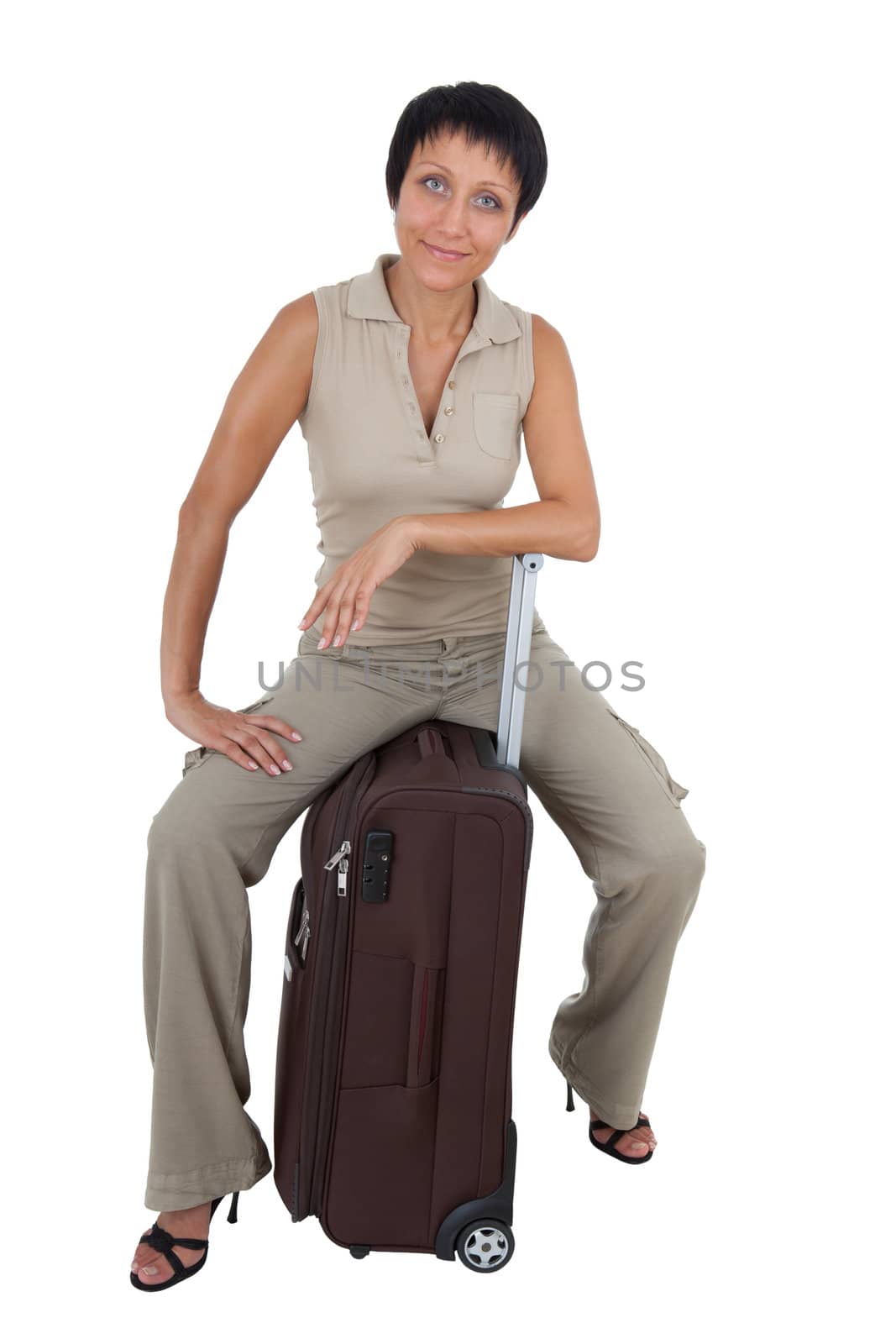 Smiling young tourist haircut woman dressed buff trouser suit sits on the  brown traveling suitcase isolated
