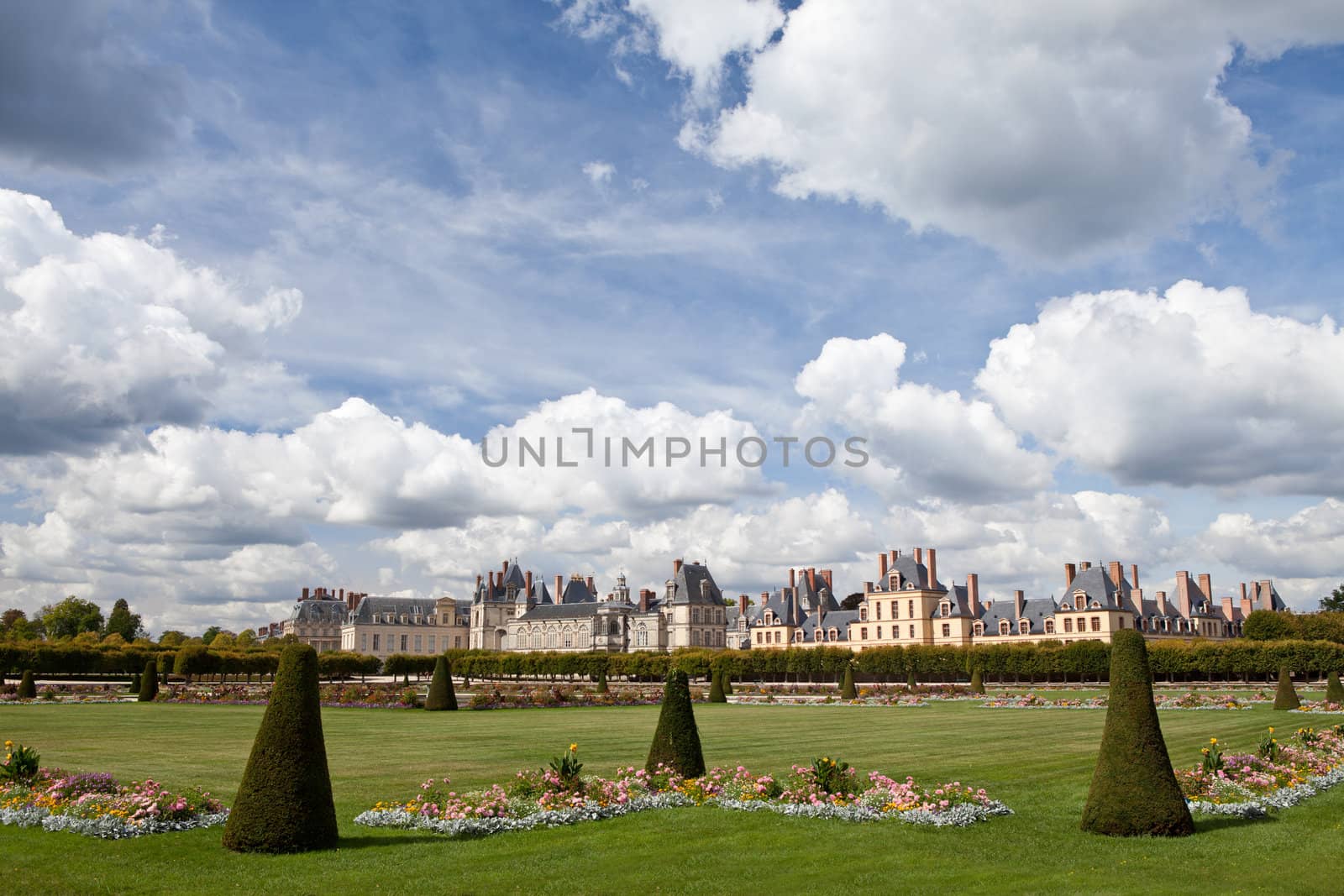 Medieval landmark royal hunting castle Fontainbleau near Paris in France and garden with flowers on the cloudy blue sky background