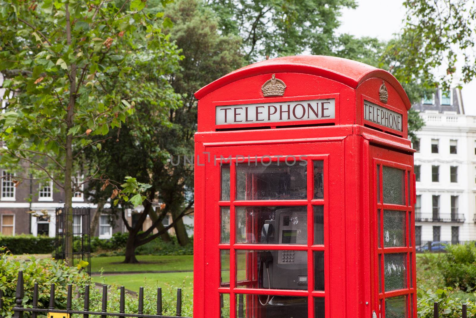 Traditional London symbol red public phone box on green park and residential district background, Great Britain