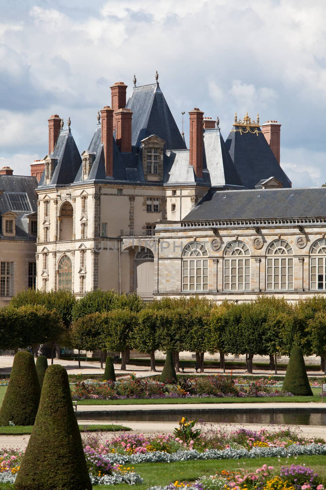 Medieval landmark royal hunting castle Fontainbleau near Paris in France and garden with flowers on the cloudy blue sky background