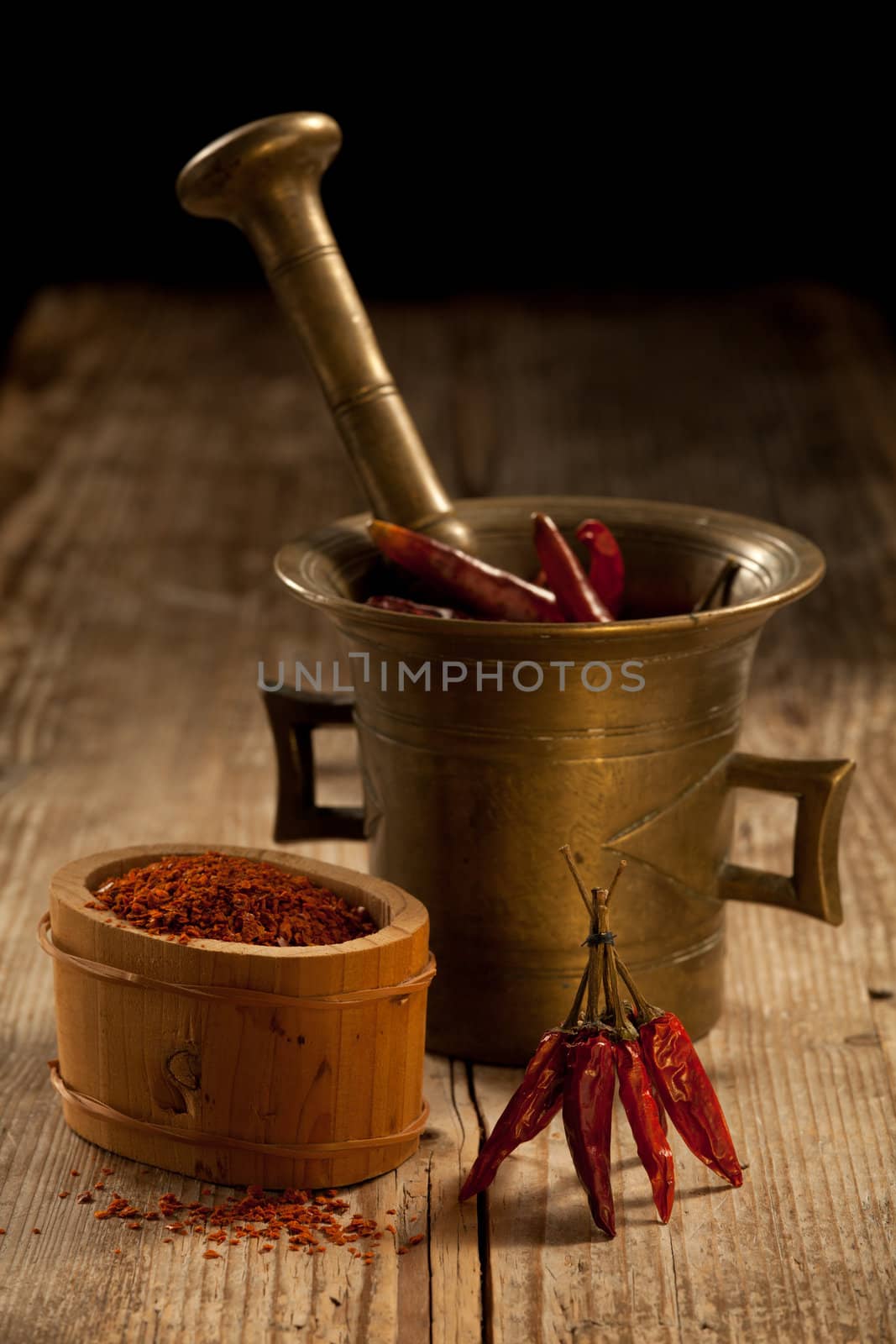 Bunch of red hot cayenne pods, bronze pounder and milled chilli pepper in wooden bowl on wooden table and black background