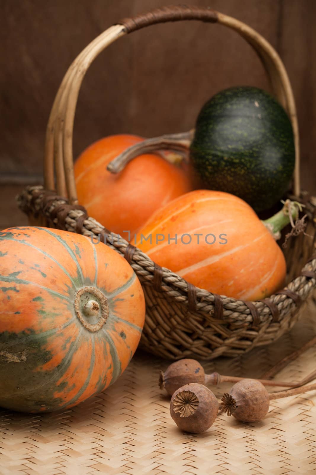 Ripe orange pumpkins in rural woven basket and poppy heads on wooden table